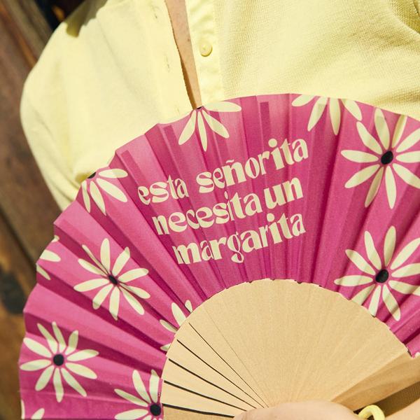 Persona usando abanico rosa con margaritas en terraza de verano